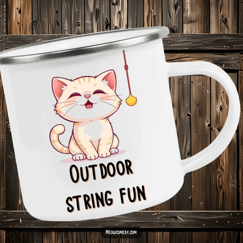Funny cat camping mug illustrating a cat joyfully batting at a dangling string toy with its paws, full of playful energy.